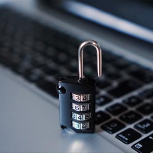 Auf diesem Bild ist ein kleiner, schwarzer Zahlenschloss-Vorhängeschloss zu sehen, das auf einer Tastatur eines Laptops platziert ist. Das Schloss ist offen, was Sicherheit und Datenschutz in der digitalen Welt suggeriert. Die Tastatur im Hintergrund zeigt an, dass das Thema um Computersicherheit oder Datenschutz in der IT-Welt kreist.